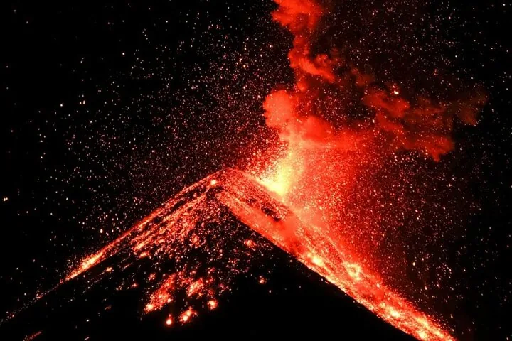 Fuego volcano erupting at night with glowing lava and sparks over its dark cone