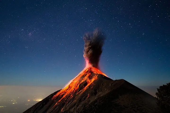 Fuego volcano erupting at night, with glowing lava on its upper slope under a starry sky