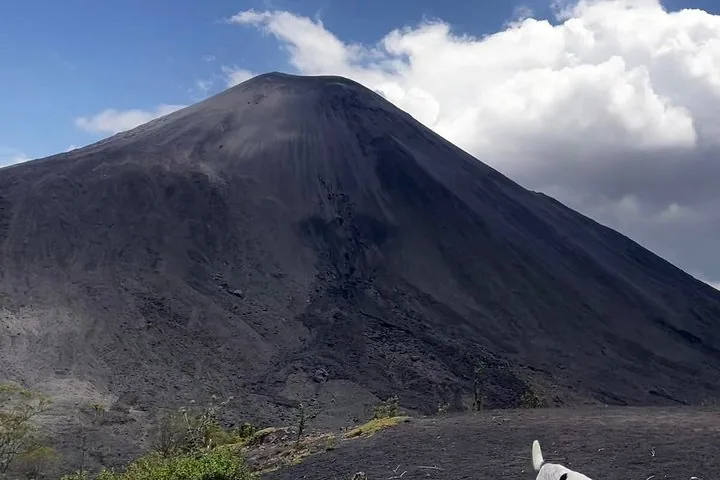 The dark, steep cone of Pacaya against a blue sky with a white cloud
