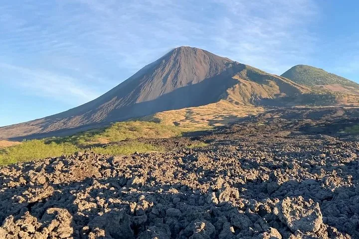 The cone of Pacaya and a second green peak above a field of black lava rock under a blue sky