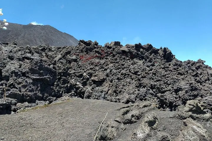 Rough black lava rock piled under a blue sky, with the volcano slope on the left